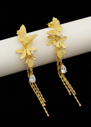 Gold butterfly earrings with chain details on a branded box background