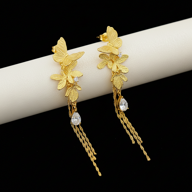 Gold butterfly earrings with chain details on a branded box background