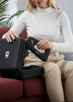 Person holding a travel-sized massage device with a visible brand logo, sitting on a couch.