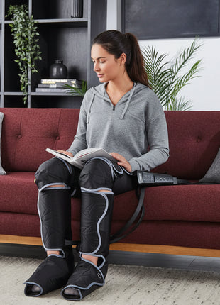 Woman sitting on a couch wearing electric leg warmers, reading a book.