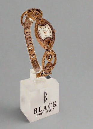 Rose gold watch on a white stand with 'Black Swiss Quartz' branding against a gray background