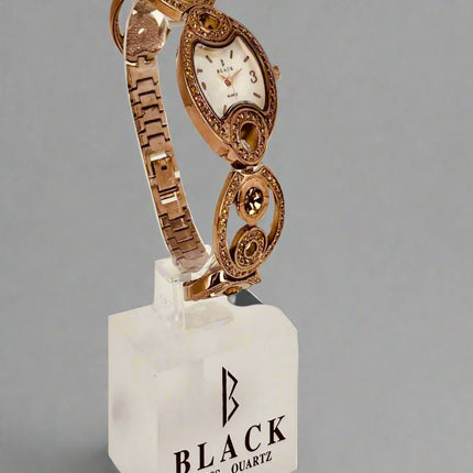 Rose gold watch on a white stand with 'Black Swiss Quartz' branding against a gray background