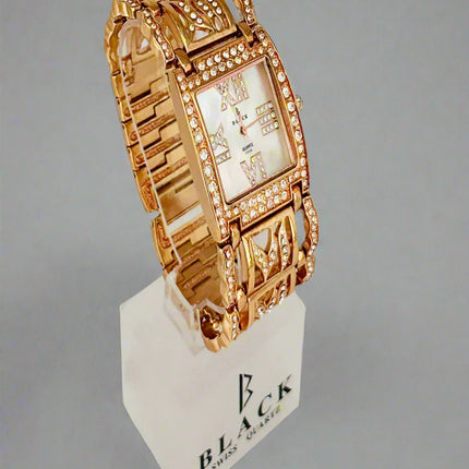 Gold wristwatch on a white stand with 'BLACK' branding against a gray background