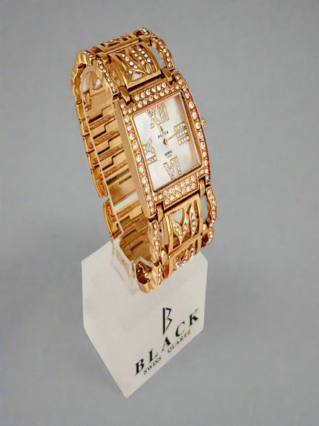 Gold wristwatch on a white stand with 'BLACK' branding against a gray background