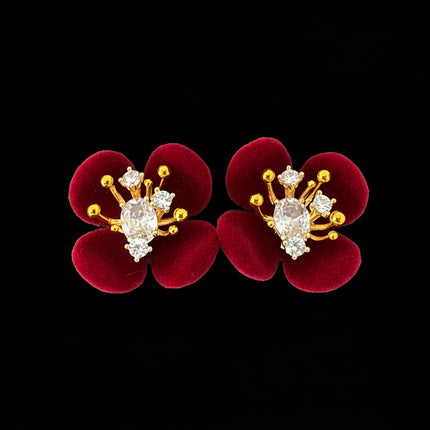 Red flower-shaped earrings with gold and diamond-like accents on a black background