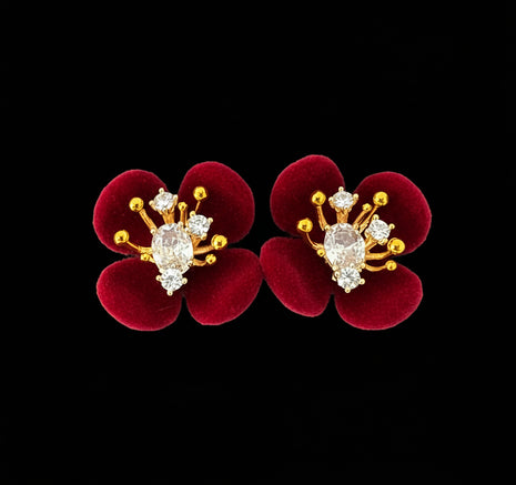 Red flower-shaped earrings with gold and diamond-like accents on a black background