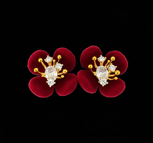 Red flower-shaped earrings with gold and diamond-like accents on a black background