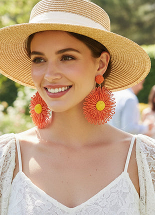 Woman wearing a straw hat and large orange earrings in a garden setting