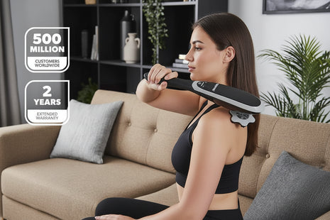 Woman using a massage device on her shoulder in a living room setting.